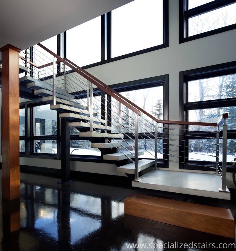 An industrial modern mono stringer with concrete treads, stainless steel cable railing and wood handrail.