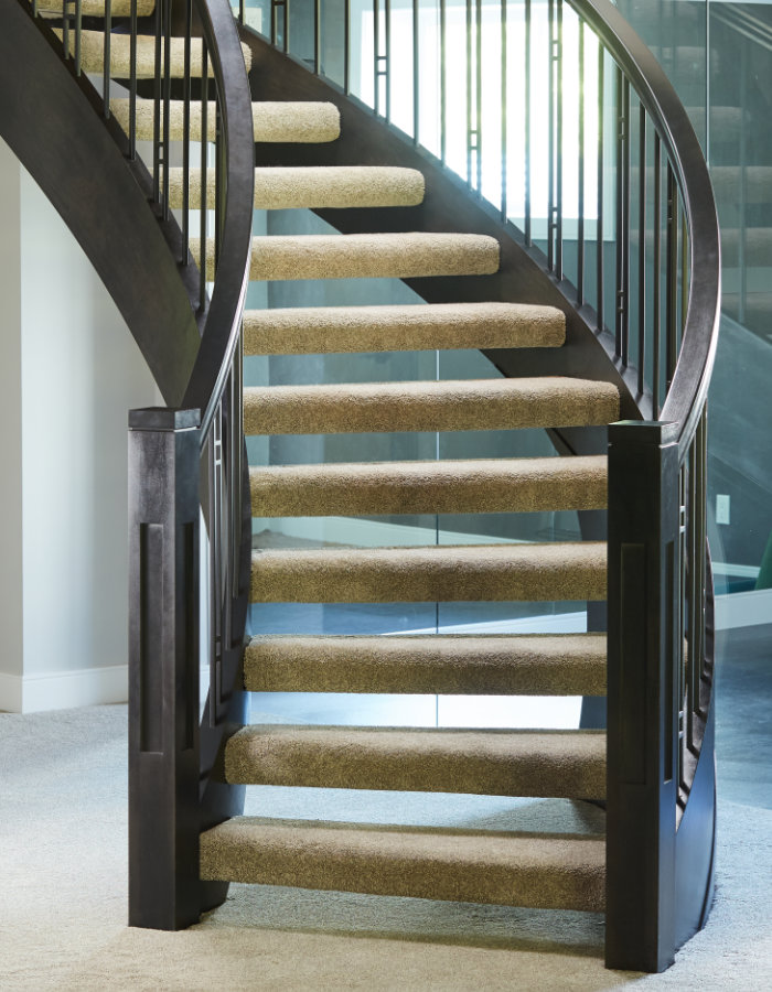 Curved open rise staircase with carpeted treads and contemporary craftsman style newel posts and spindles.