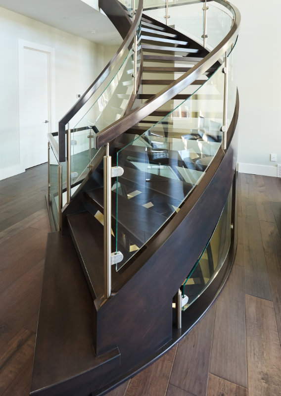 A dark brown maple open rise curved staircase with clamped glass railing.