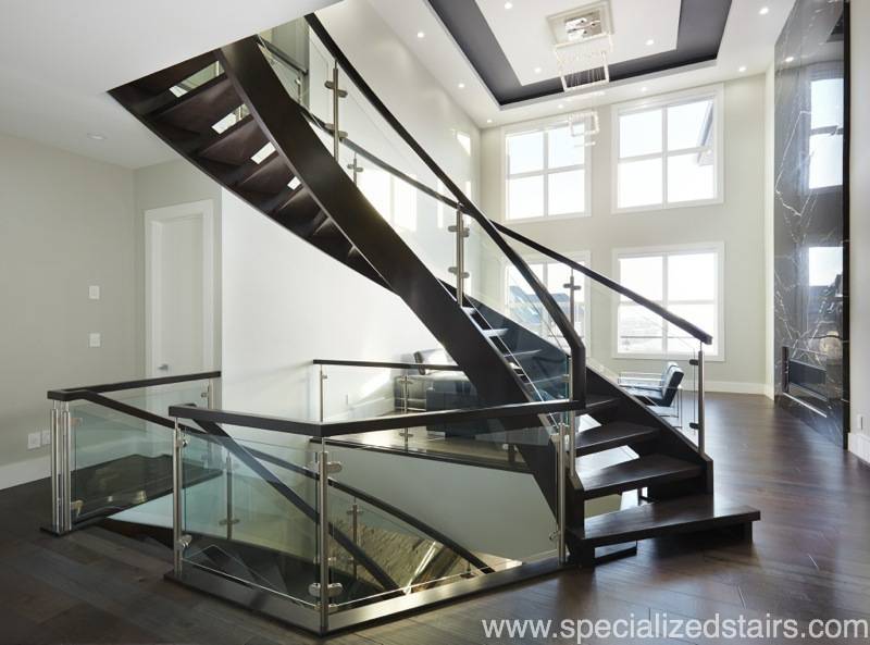 A curved maple open rise staircase with glass railng and maple handrail leading from the second floor to the main floor. The railing continues around to meet the staircase leading to the basement.