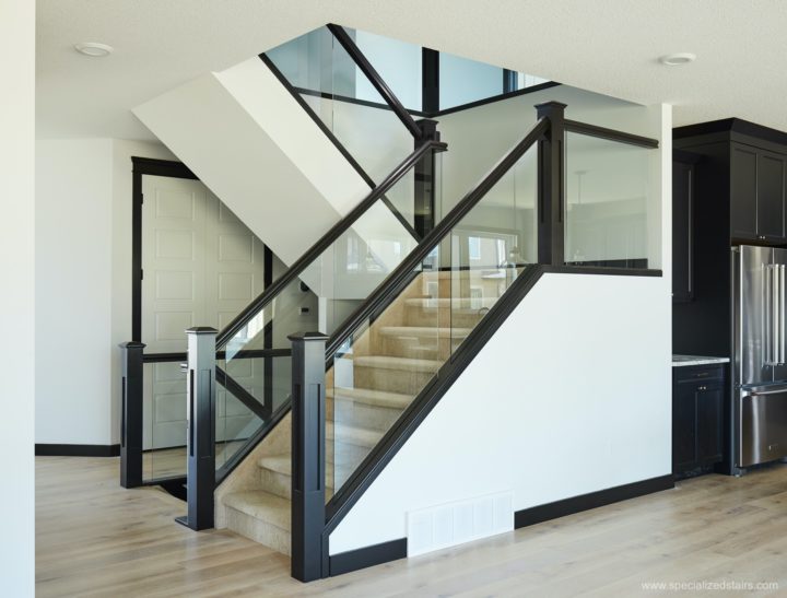 A u-shaped staircase with dark brown wood newel posts and handrails, glass panel railing and carpeted treads.